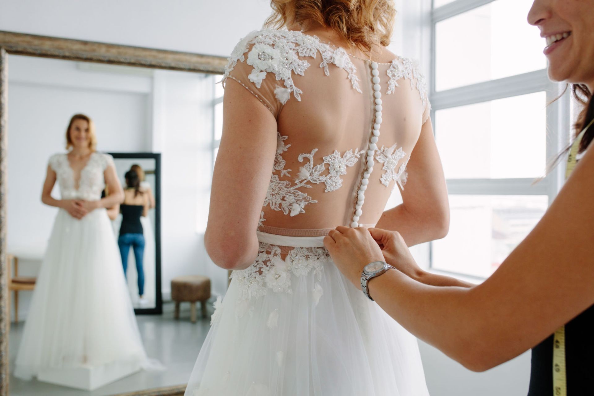 Bridal gown fitting with lace details and buttons, reflected in a mirror.